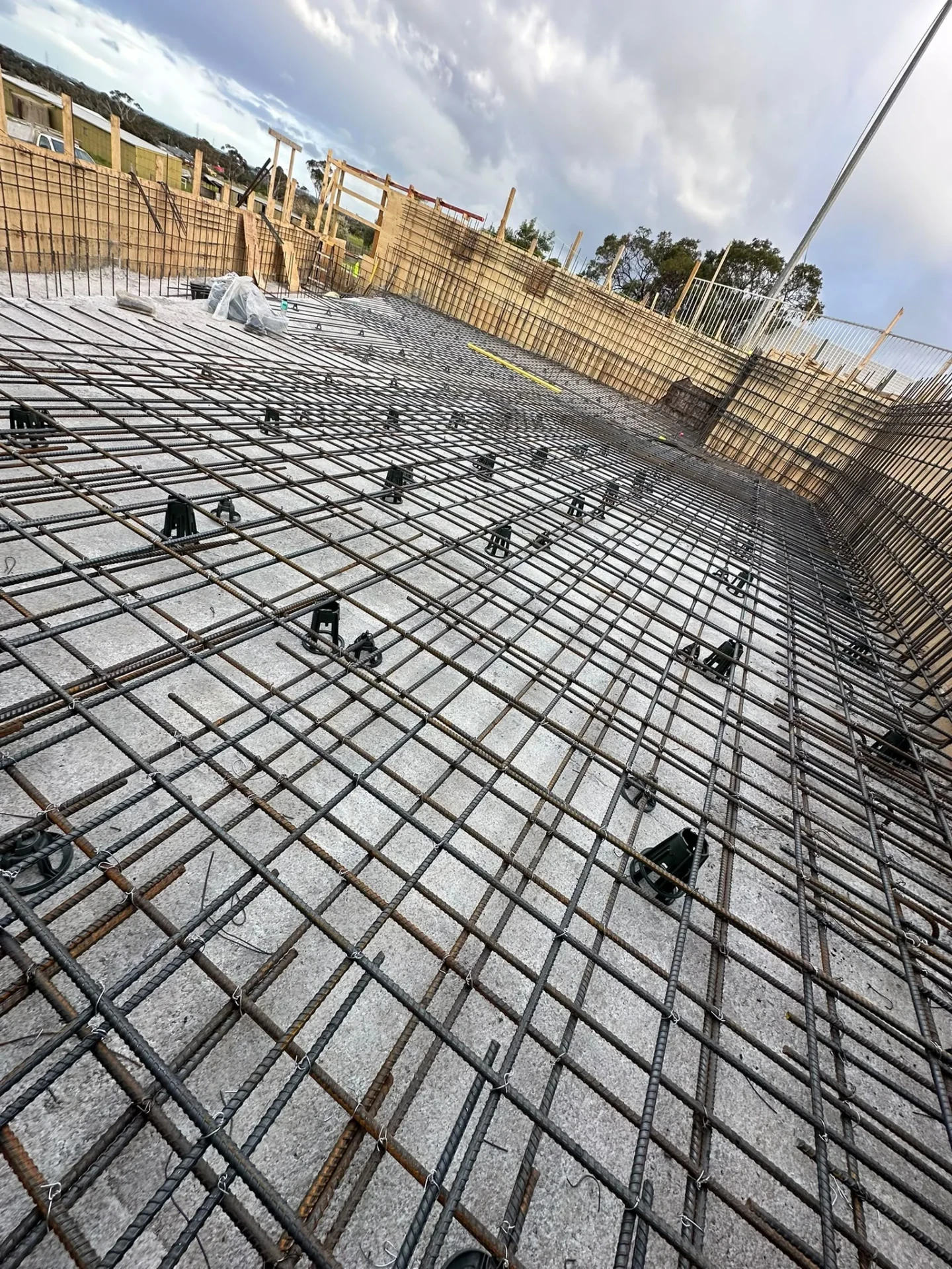 Large pool floor covered with layered steel reinforcement on bar chairs, framed by timber formwork walls.