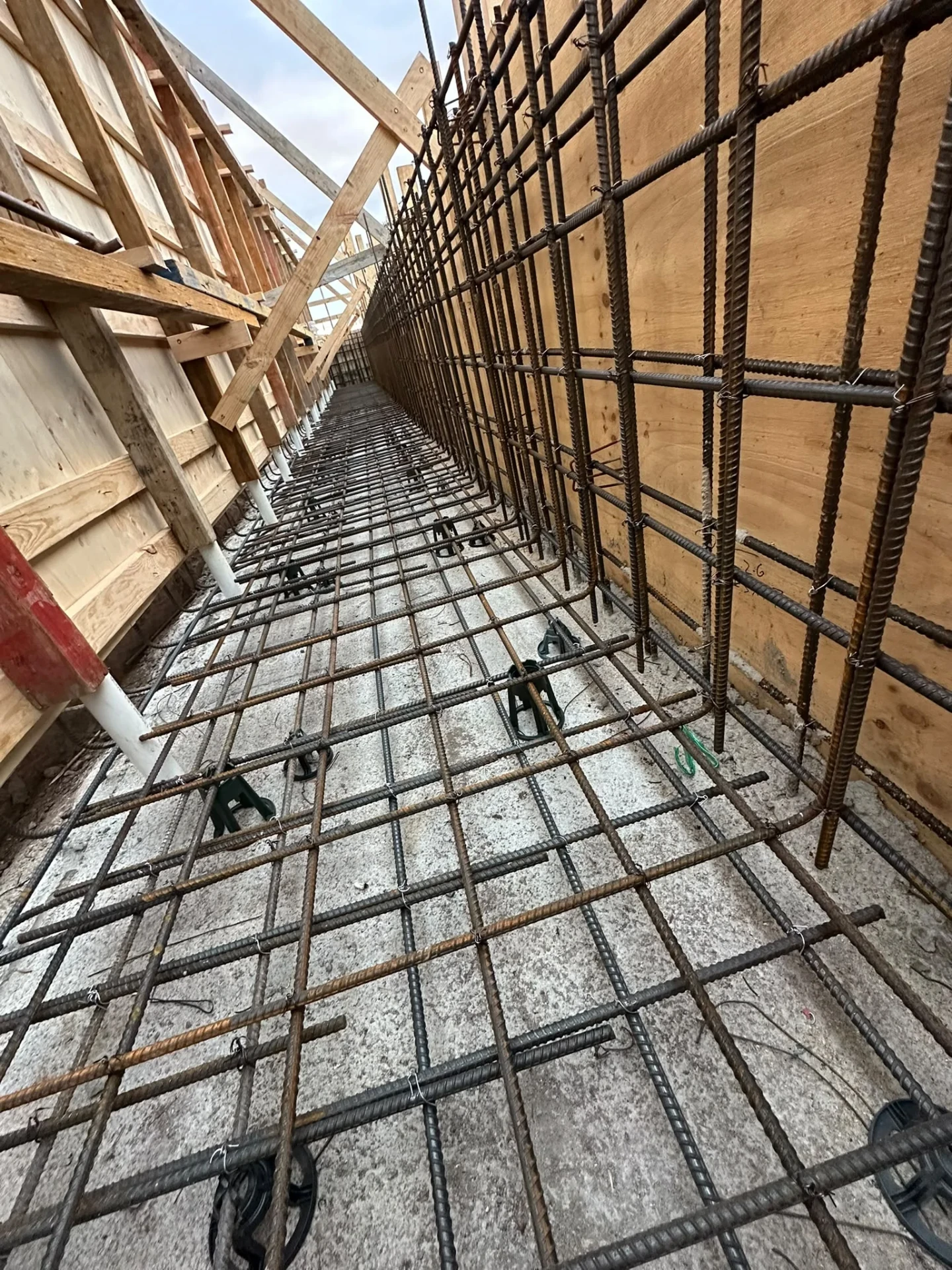 Long narrow pool section with braced timber formwork, wall reinforcement and vertical service pipes running along the base.