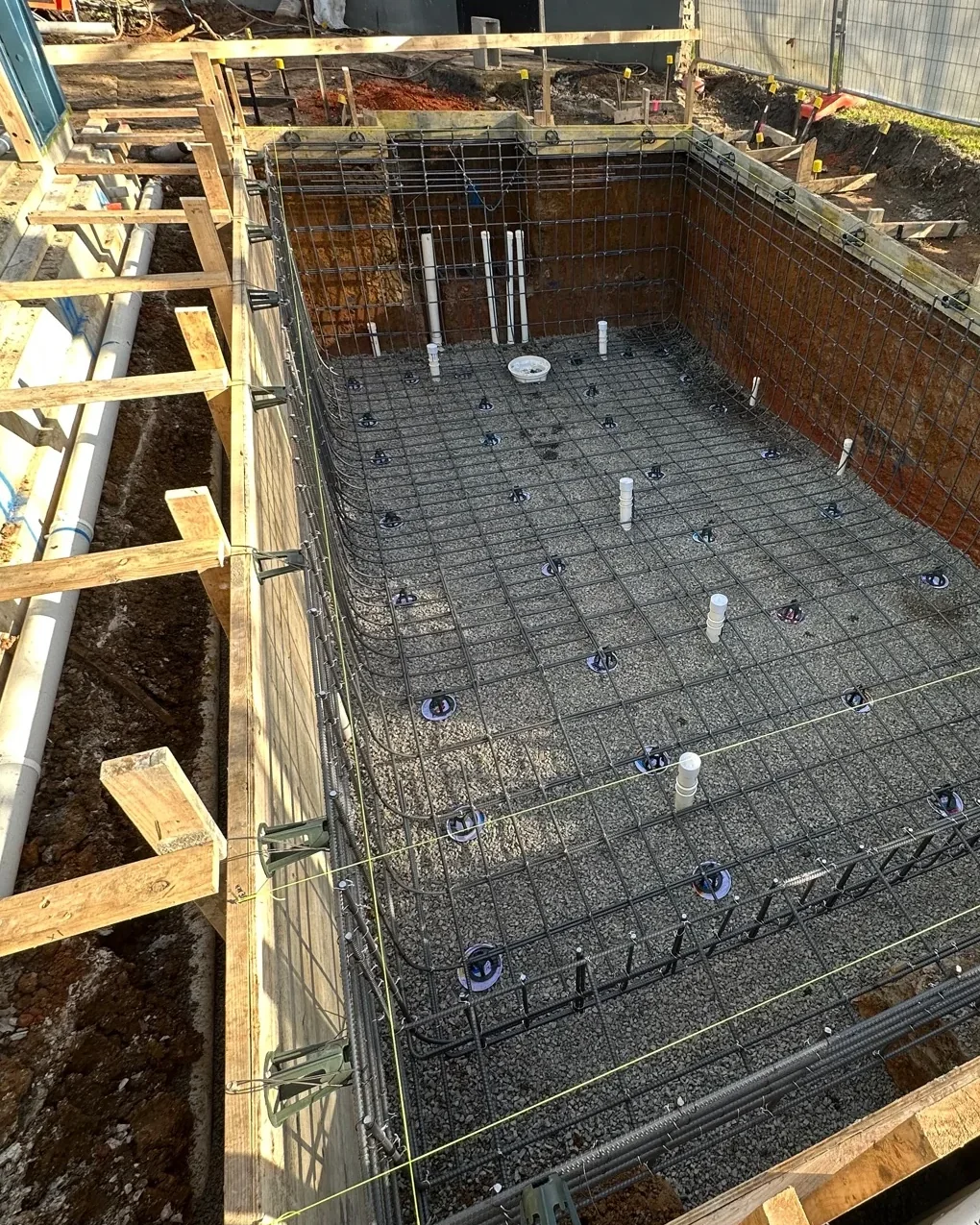 Whole compact rectangular pool with floor and wall reinforcement integrated beside an active building structure.